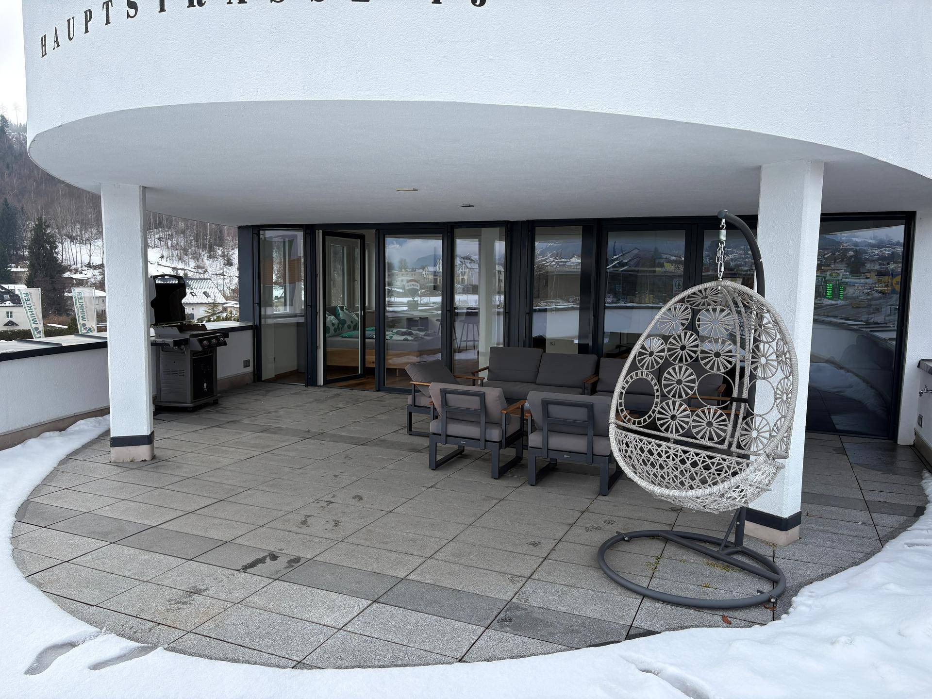 Überdachte Terrasse mit Lounge-Möbeln, Hängesessel und Grill, ideal für entspannte Stunden im Freien.