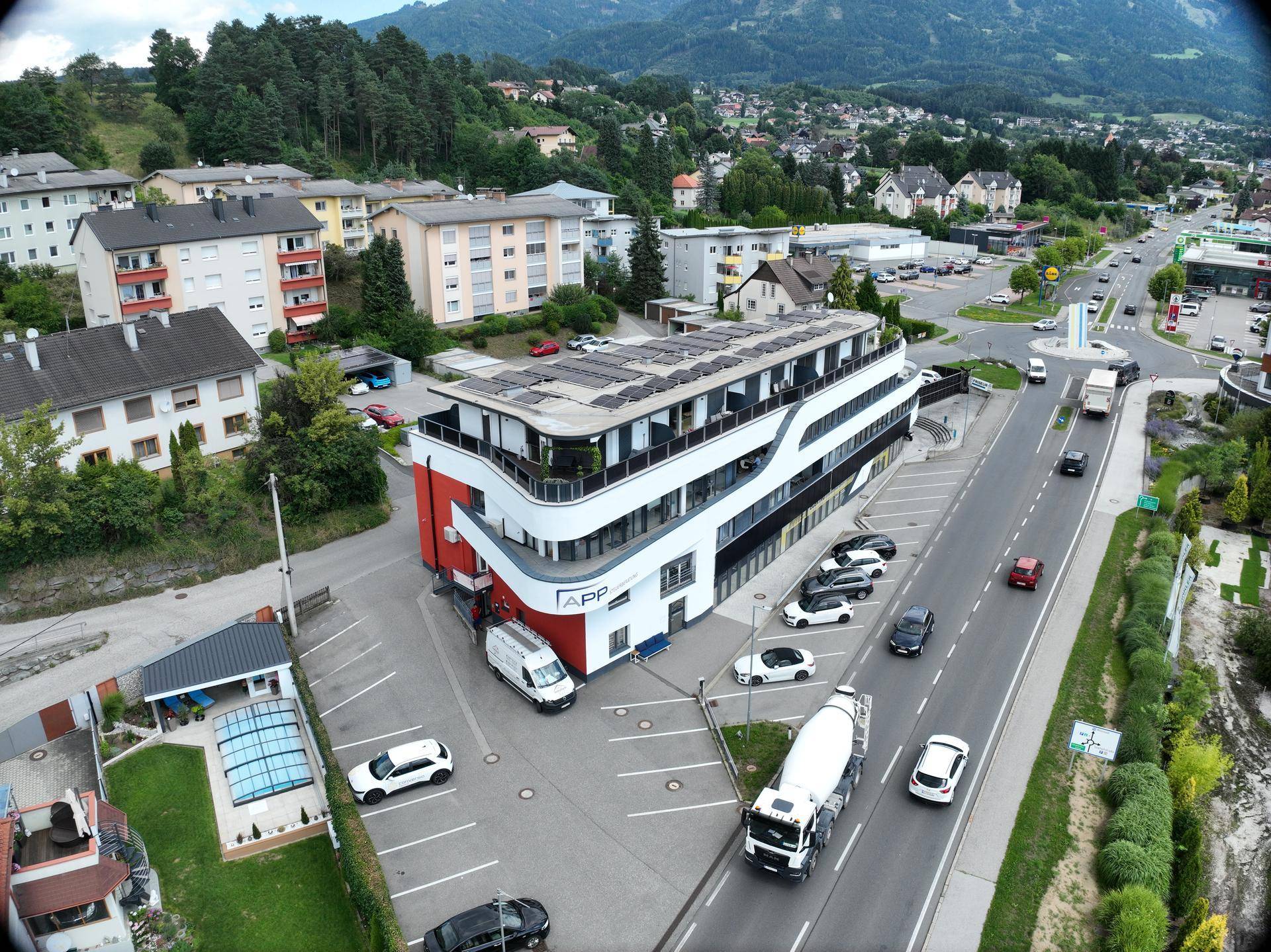 Panoramablick aus der Luft auf ein modernes Gebäude mit Photovoltaikanlage und der umliegenden Stadtlandschaft.