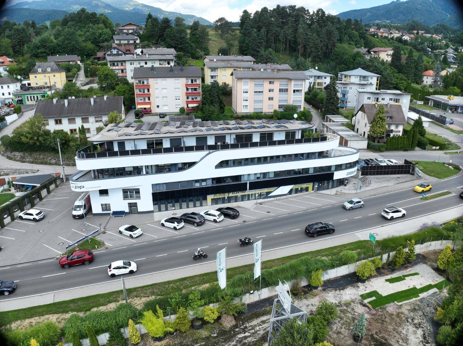 Luftaufnahme der modernen Gewerbeimmobilie an der Hauptstraße mit umliegenden Gebäuden und Natur.