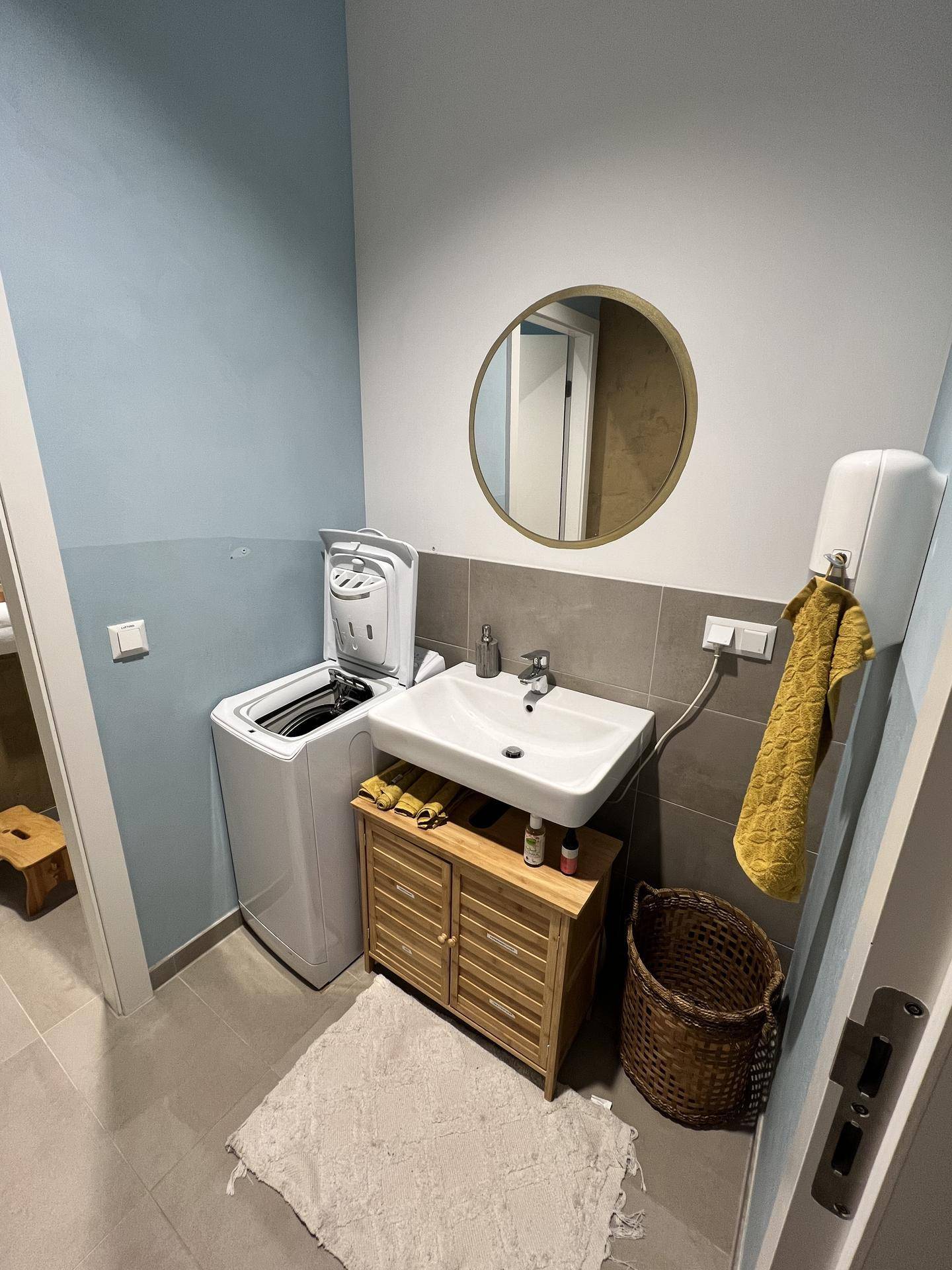 Badezimmer mit Waschbecken, Spiegel, Waschmaschine und hellblauen Wänden, funktional eingerichtet.