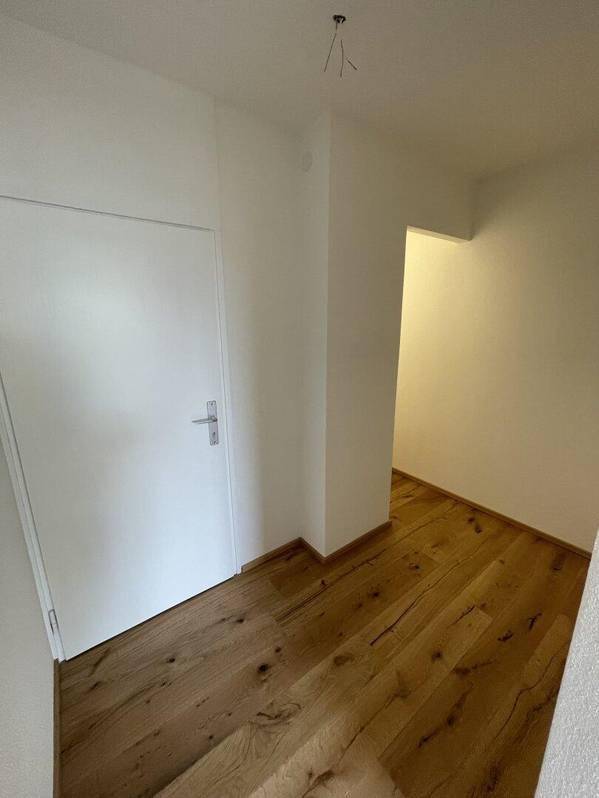Heller Flur mit Holzboden und weißer Tür, der zu weiteren Räumen führt.