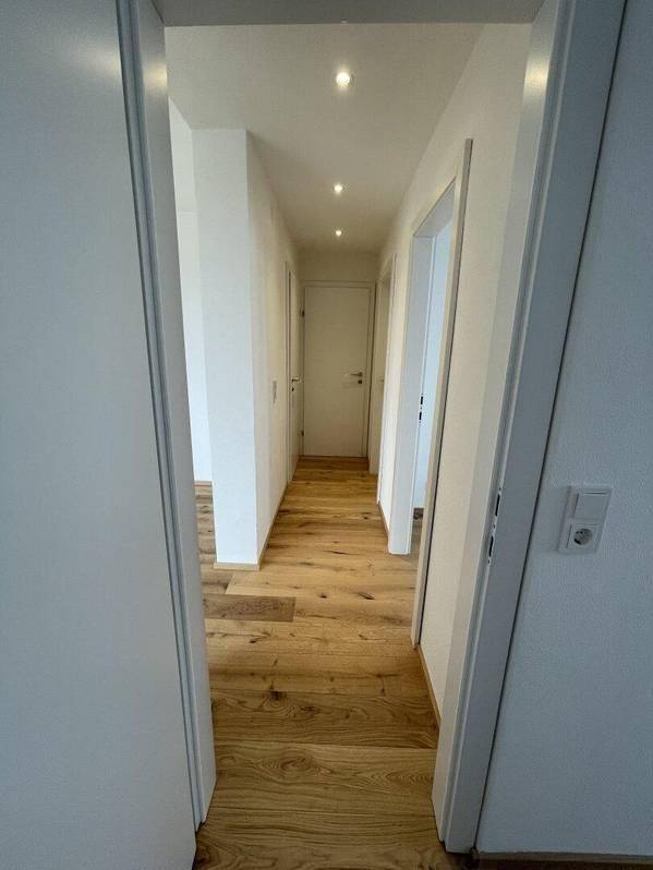 Langer, heller Flur mit Holzboden und Einbaustrahlern, der verschiedene Zimmer verbindet.