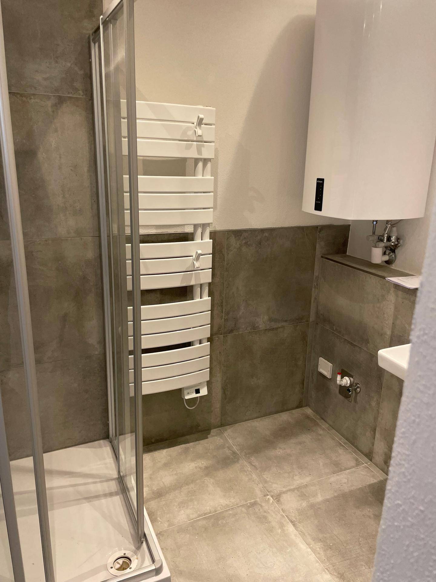 Badezimmer mit Duschkabine, beheiztem Handtuchhalter und modernem Warmwasserbereiter.