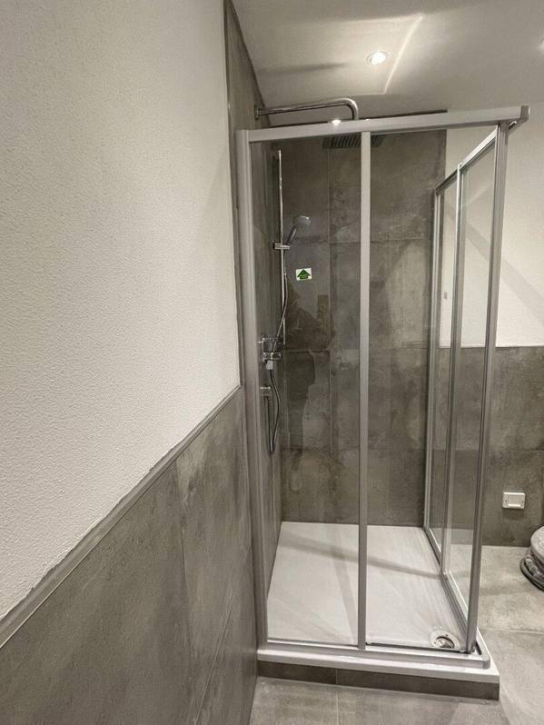 Moderne Duschkabine in einem Badezimmer mit grauen Fliesen und minimalistischem Design.