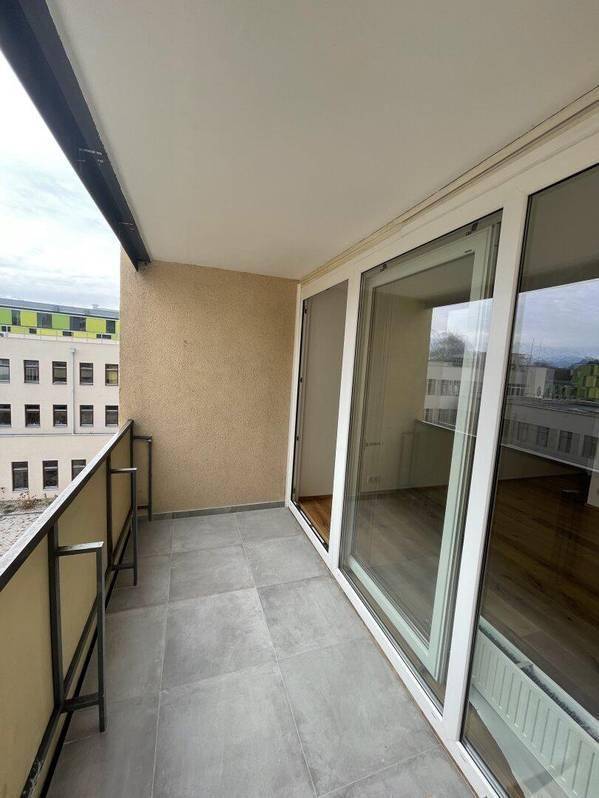 Geräumiger Balkon mit grauen Fliesen und Metallgeländer, bietet Blick auf umliegende Gebäude.