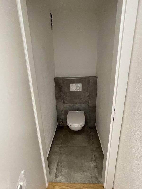 Separates WC mit wandhängender Toilette und grauen Fliesen, funktional und modern.