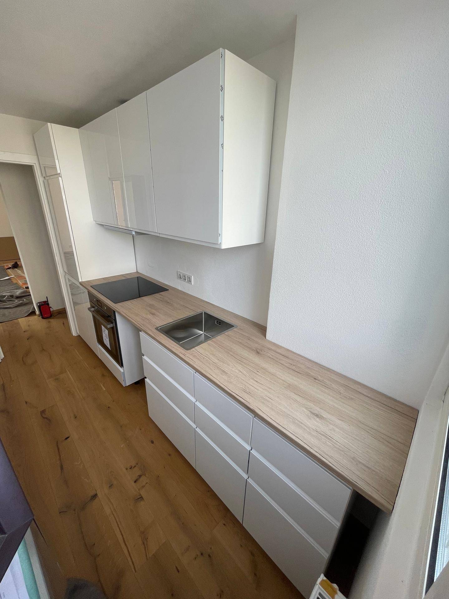 Helle Einbauküche mit weißen Hochglanzfronten und heller Holzarbeitsplatte, sehr funktional.