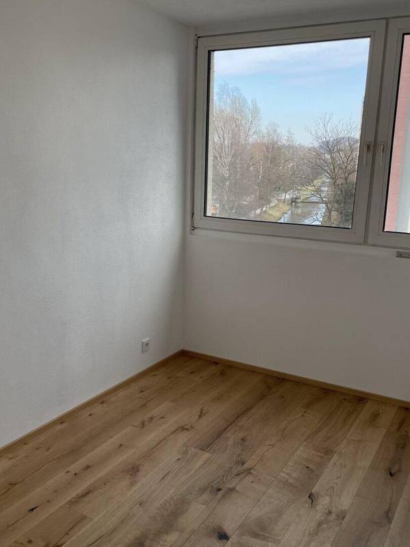 Ruhiges Zimmer mit Holzboden und Fenster, das einen angenehmen Blick ins Grüne bietet.