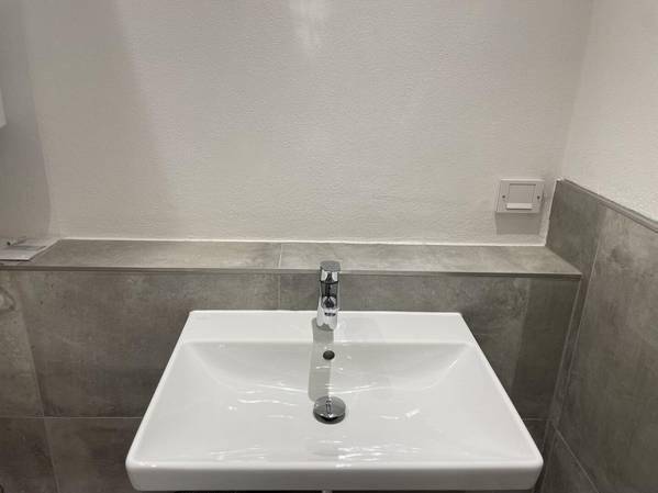 Modernes Einzelwaschbecken in einem Badezimmer mit grauen Fliesen und weißer Wand.
