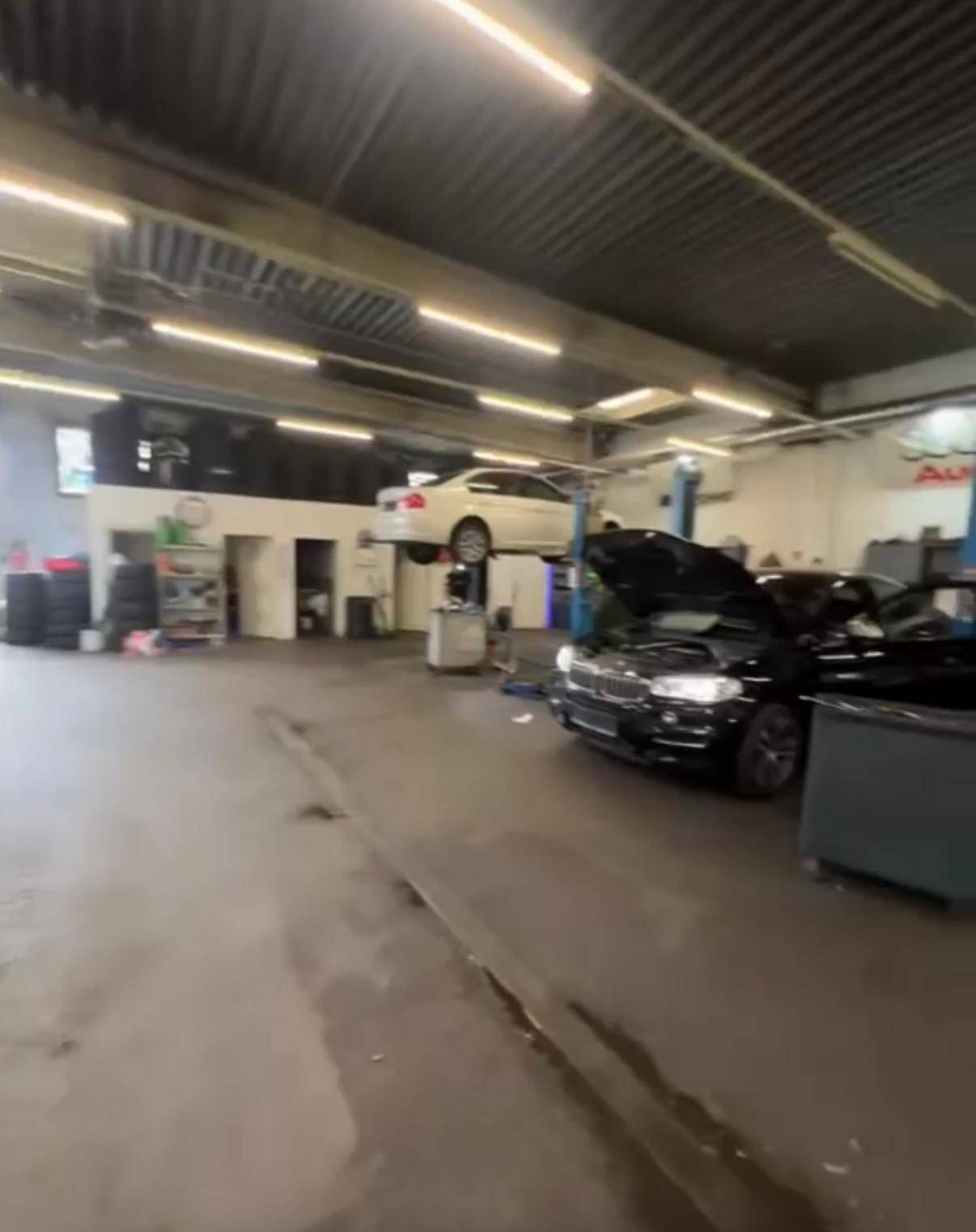 Weitläufige Autowerkstatt mit mehreren Arbeitsbereichen und Fahrzeugen auf Hebebühnen und am Boden.