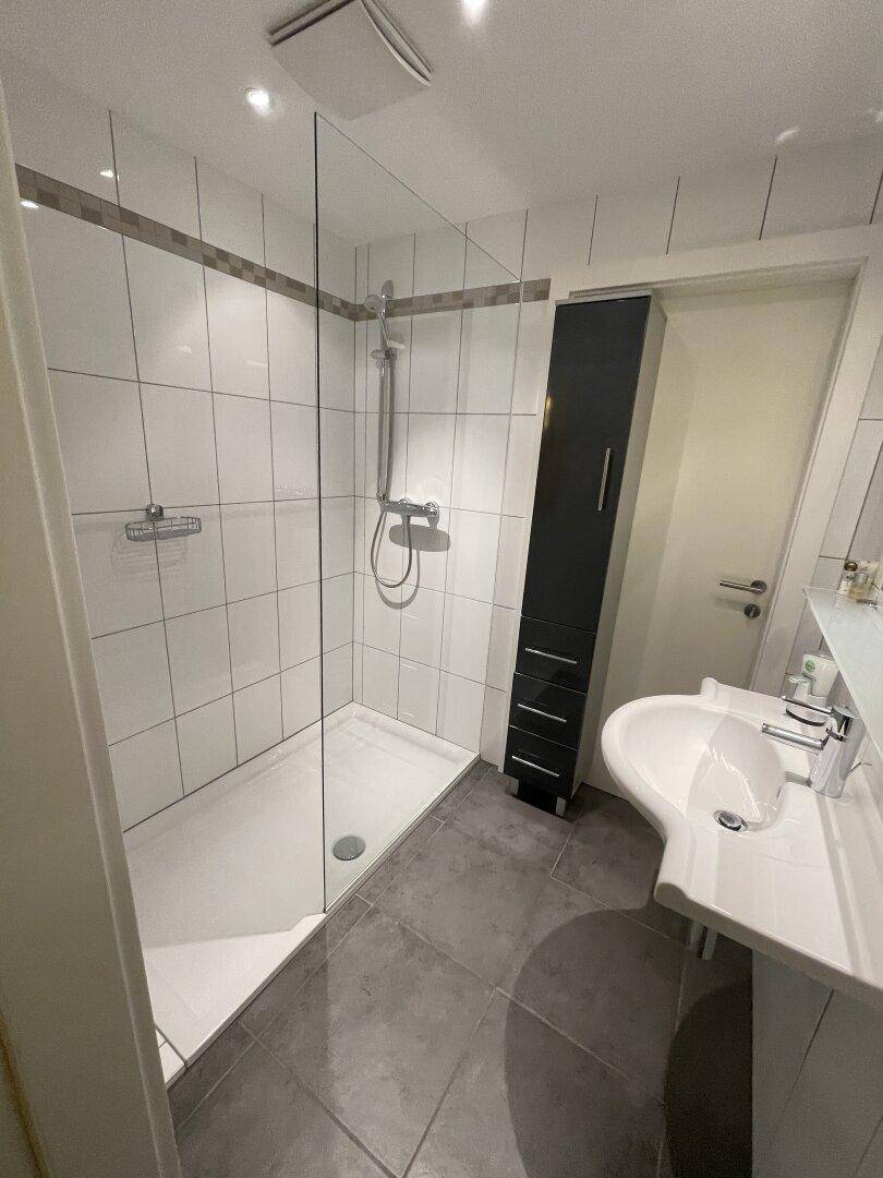 Modernes Badezimmer mit ebenerdiger Dusche, weißen Fliesen und Einzelwaschbecken.