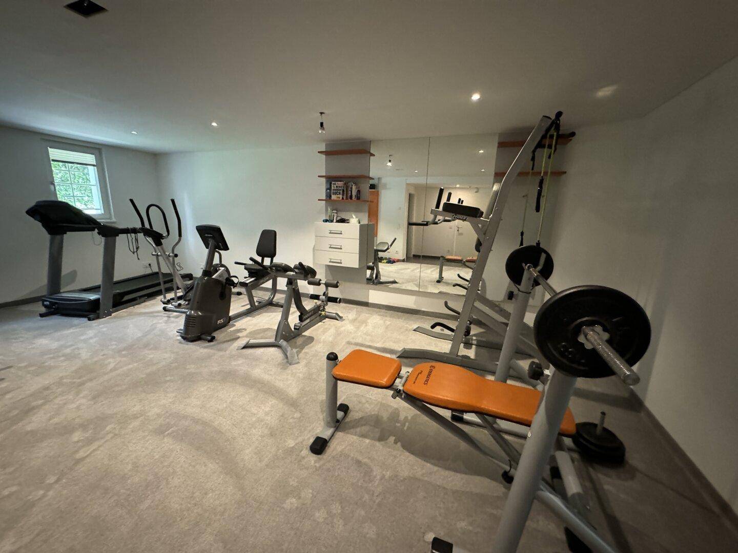 Gut ausgestatteter Fitnessraum im Untergeschoss mit verschiedenen Trainingsgeräten und Spiegelwand.