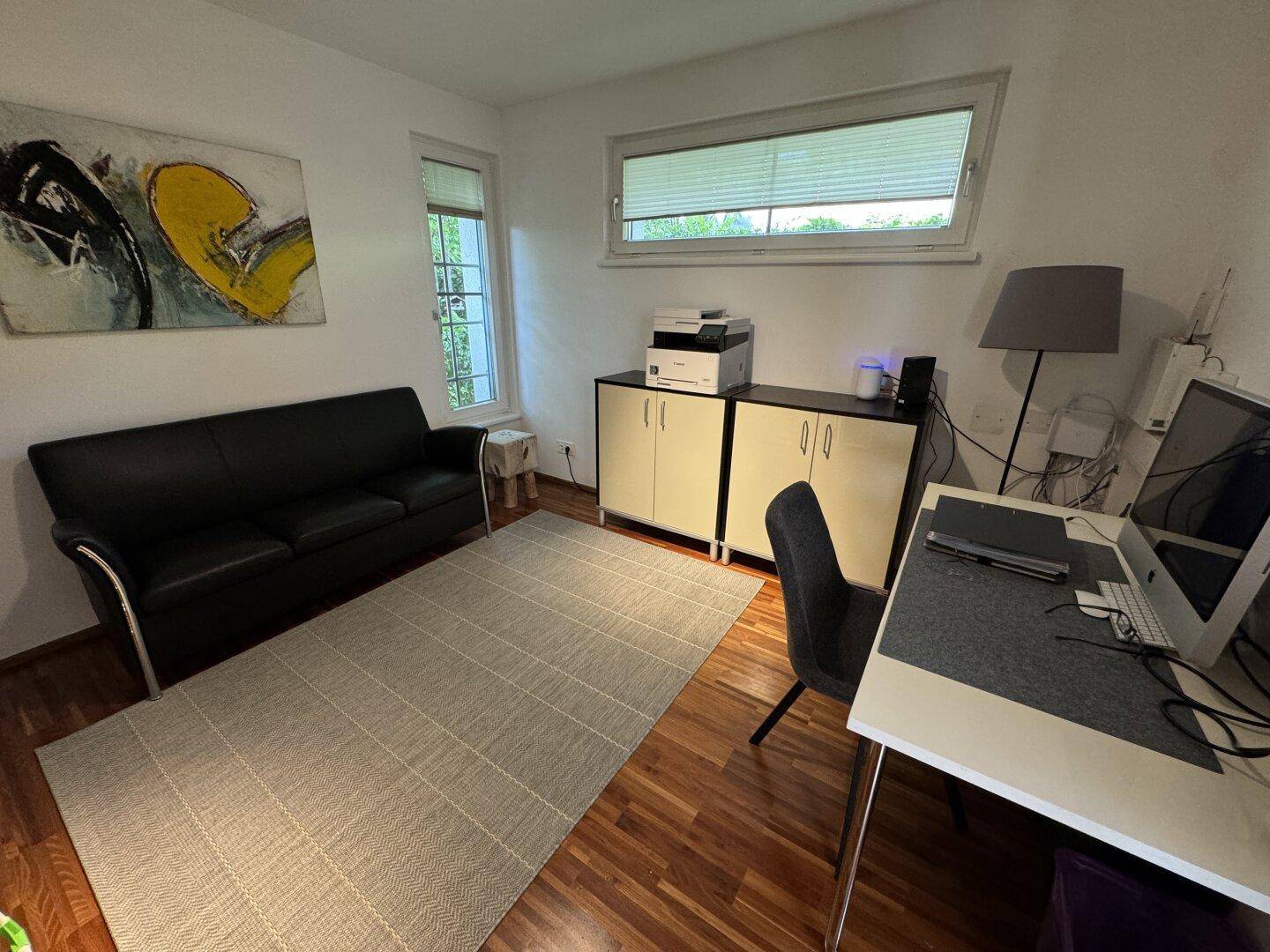 Helles Arbeitszimmer mit Schreibtisch, Sofa und Blick ins Grüne durch das Fenster.