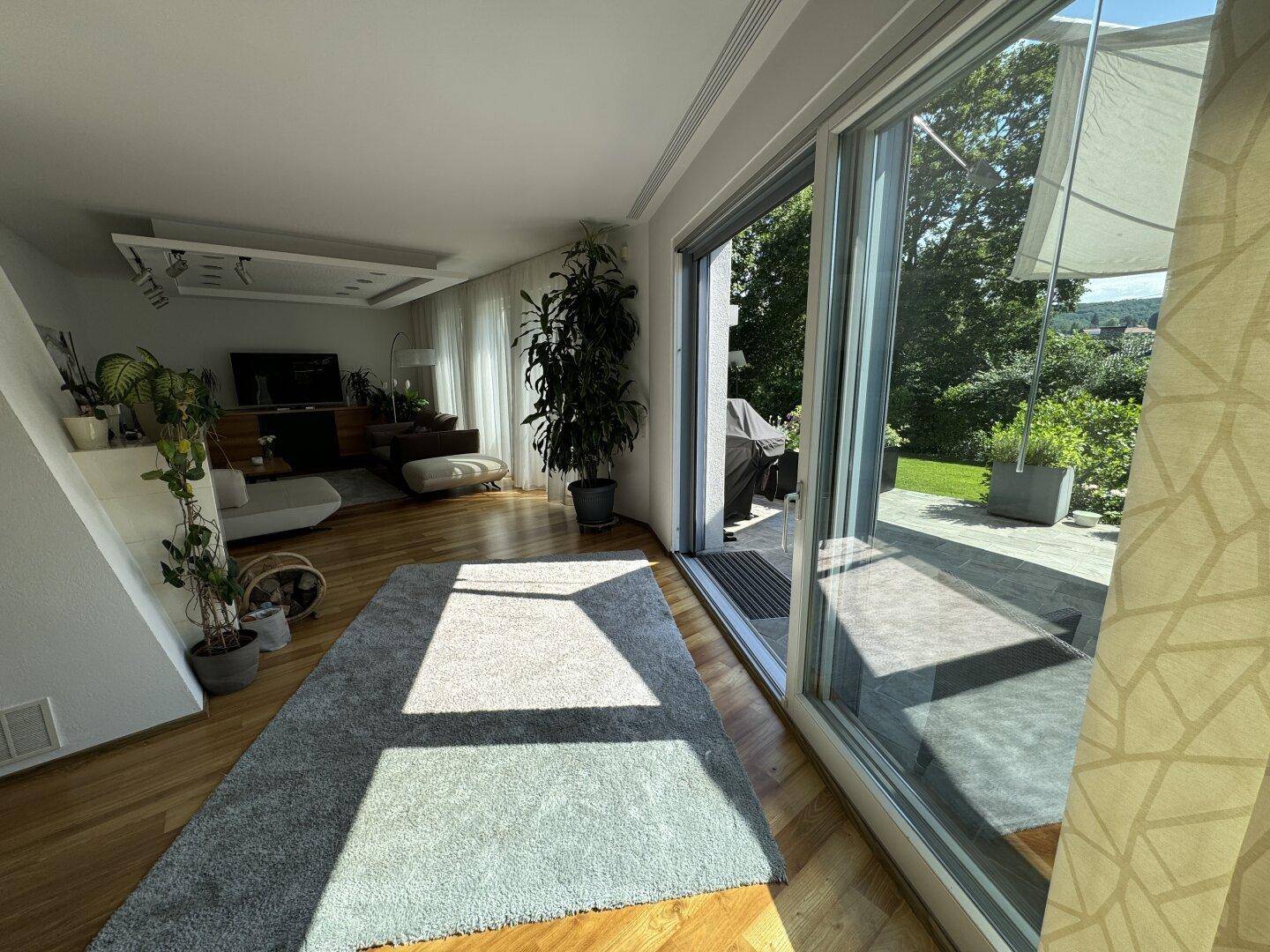 Lichtdurchflutetes Wohnzimmer mit großen Schiebetüren zum Garten und elegantem Holzboden.
