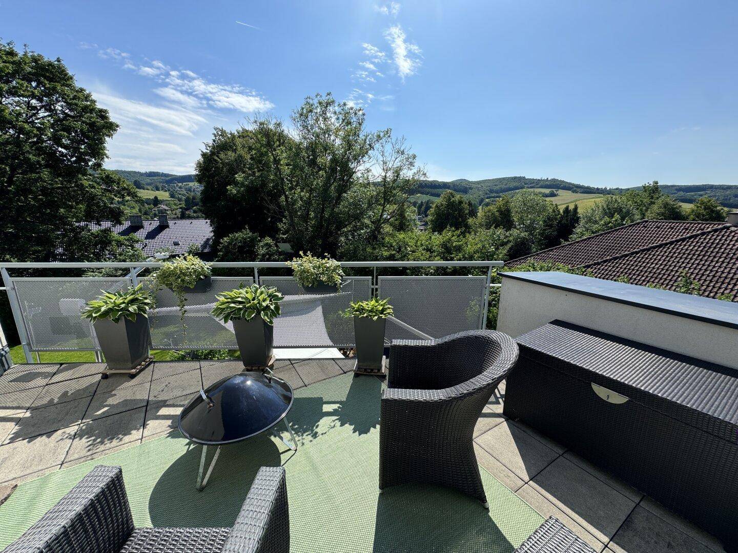 Sonniger Balkon mit Sitzgelegenheiten und weitem Blick über die grüne Landschaft.