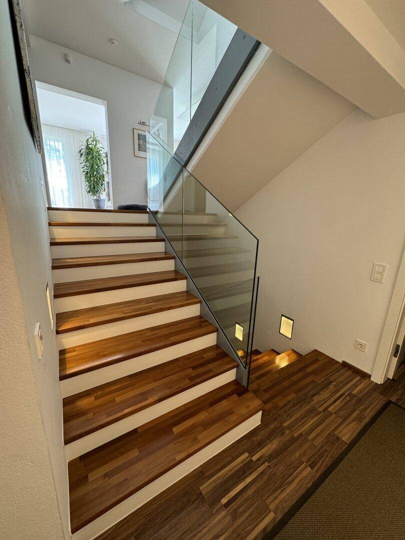 Moderne Holztreppe mit Glasgeländer und indirekter Beleuchtung im Eingangsbereich.