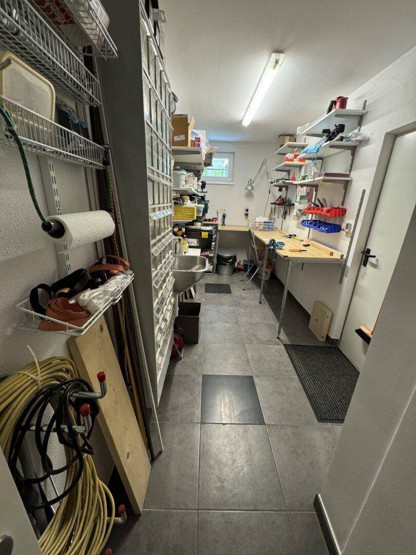 Funktionale Werkstatt mit Arbeitsflächen, Regalen und Waschbecken im Untergeschoss.