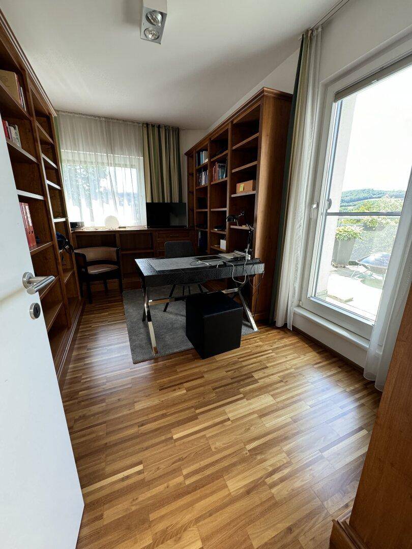 Helles Arbeitszimmer mit großem Bücherregal, Schreibtisch und Balkonzugang.
