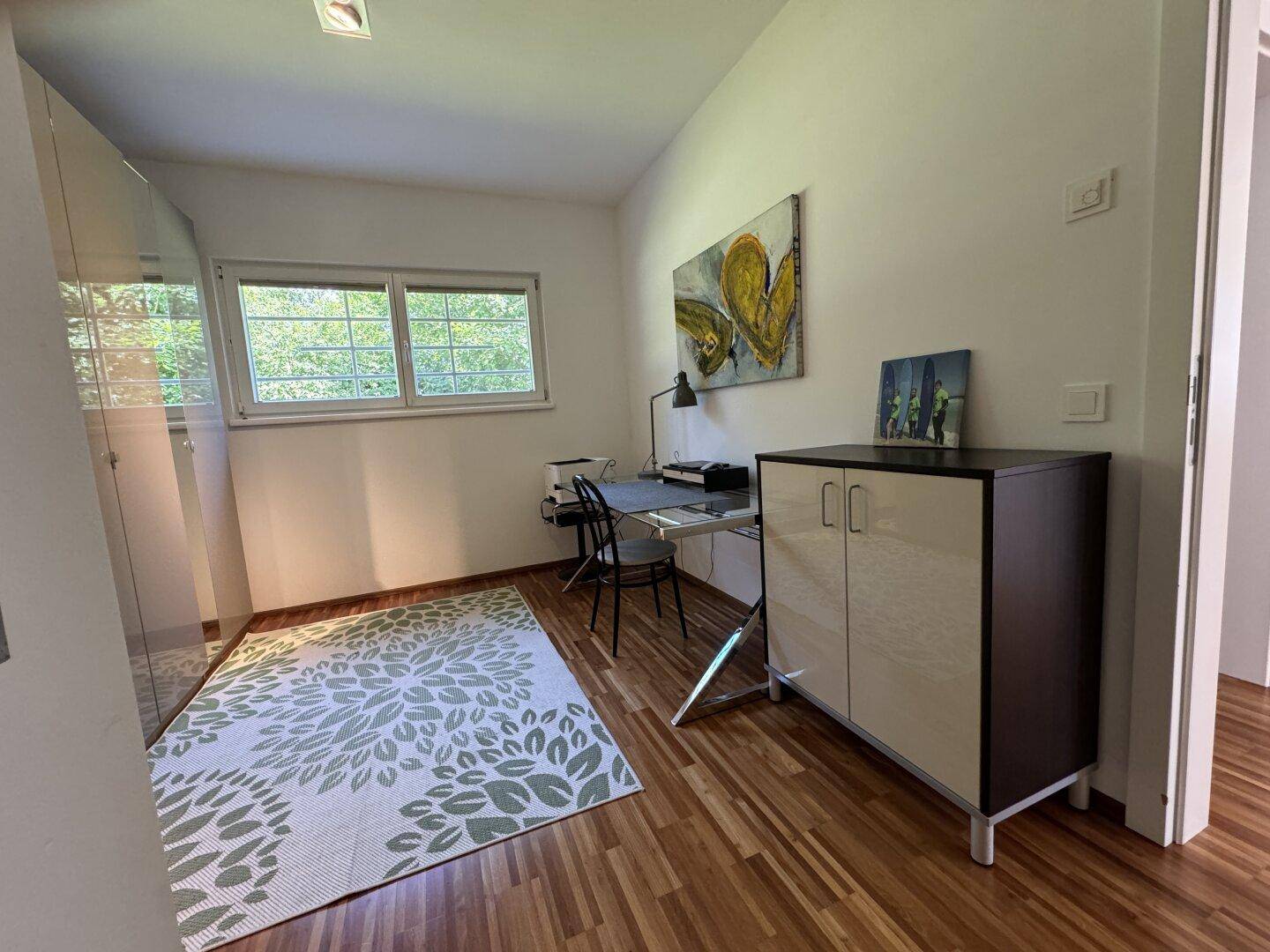 Helles Arbeitszimmer mit Holzboden, Schreibtisch und Blick ins Grüne.