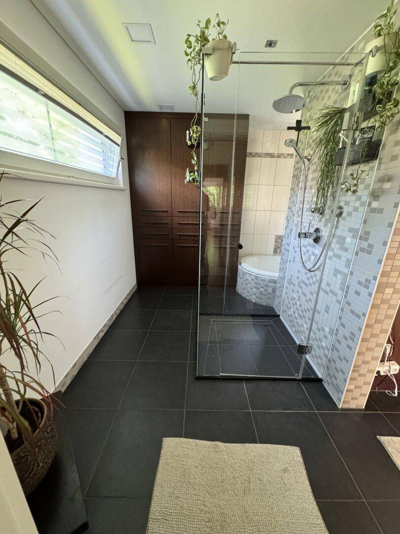 Geräumiges Badezimmer mit großer Dusche, Badewanne und dunklen Bodenfliesen sowie Fenster.