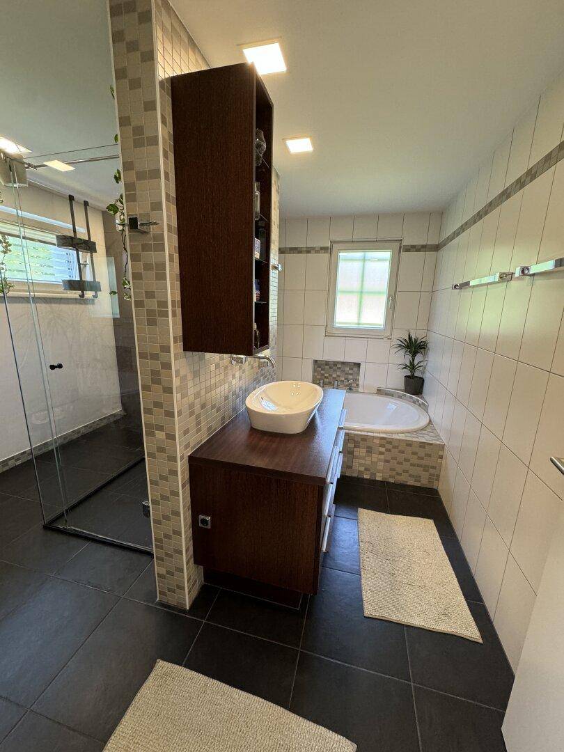 Modernes Badezimmer mit Badewanne, Dusche, Einzelwaschbecken und Fenster für Tageslicht.
