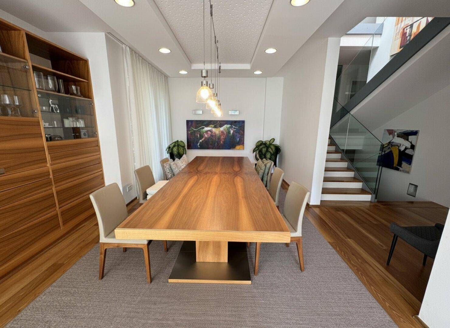 Eleganter Essbereich mit großem Holztisch, passendem Sideboard und Blick auf die Treppe.