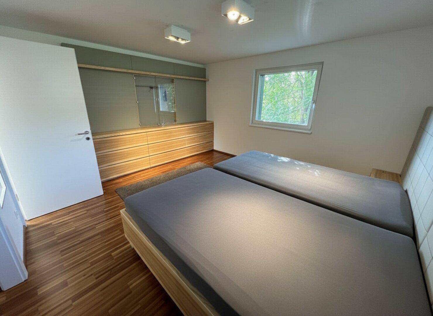 Helles Schlafzimmer mit Holzboden, zwei Einzelbetten und integrierten Einbauschränken.