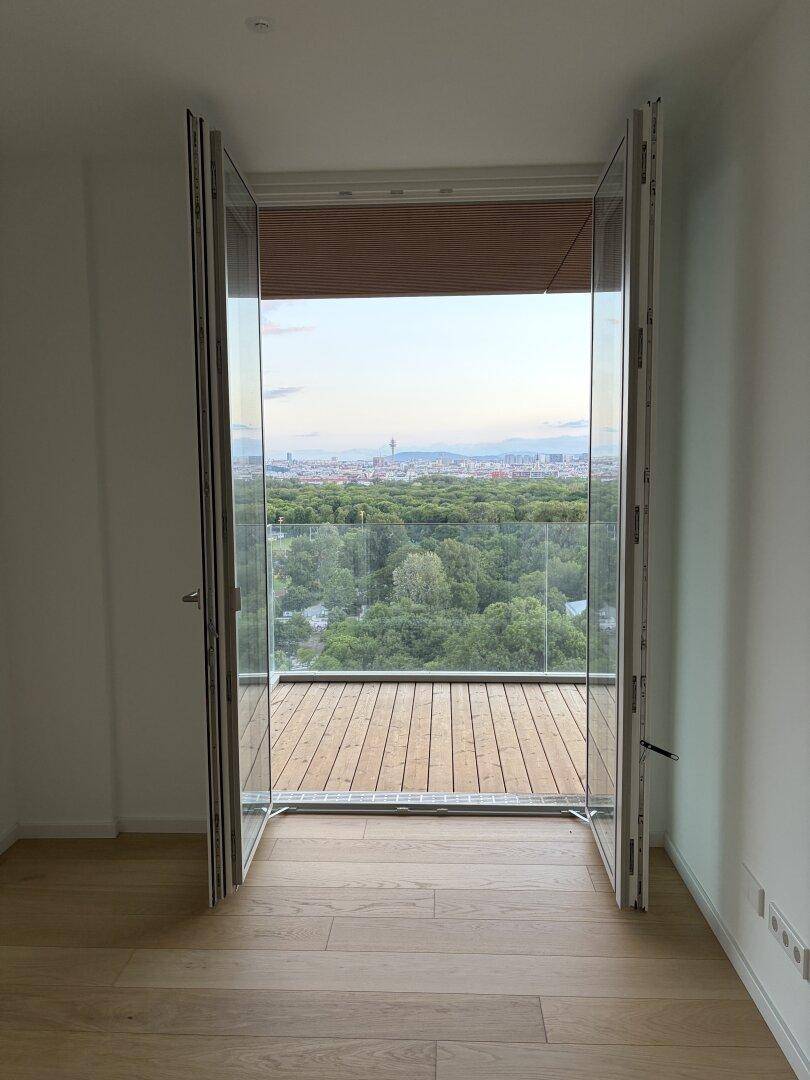 Heller Innenraum mit Zugang zu einem Balkon und weitem Blick über die Stadt und Natur.