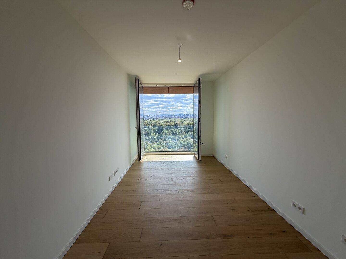 Geräumiger, leerer Raum mit Parkettboden und Panoramafenstern mit Blick auf die Skyline und Natur.