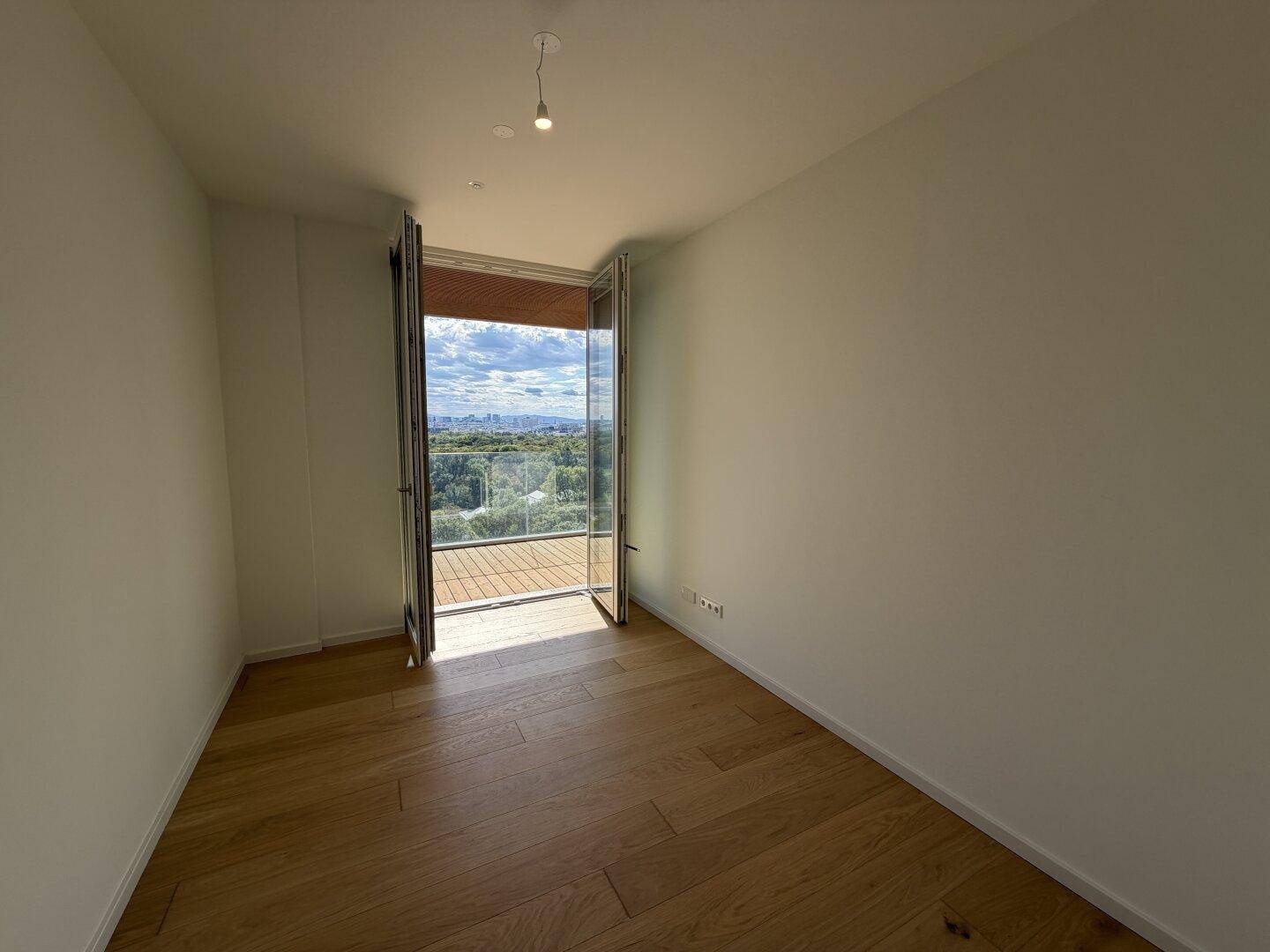 Lichtdurchfluteter Raum mit hellem Holzboden und Zugang zu einem Balkon mit Fernsicht.