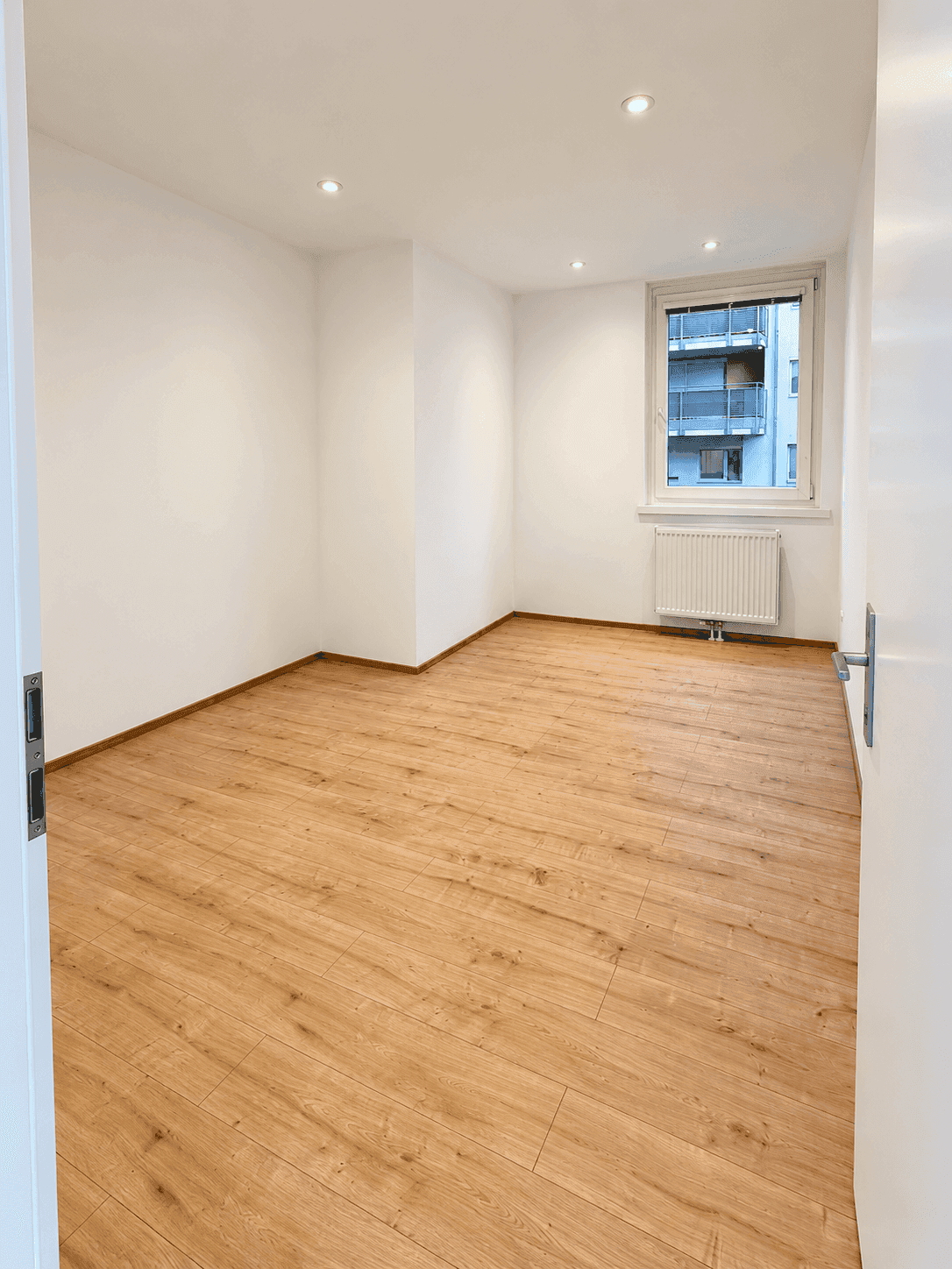 Geräumiges, unmöbliertes Zimmer mit hellem Laminatboden und Blick auf den Innenhof, bereit zum Einrichten.