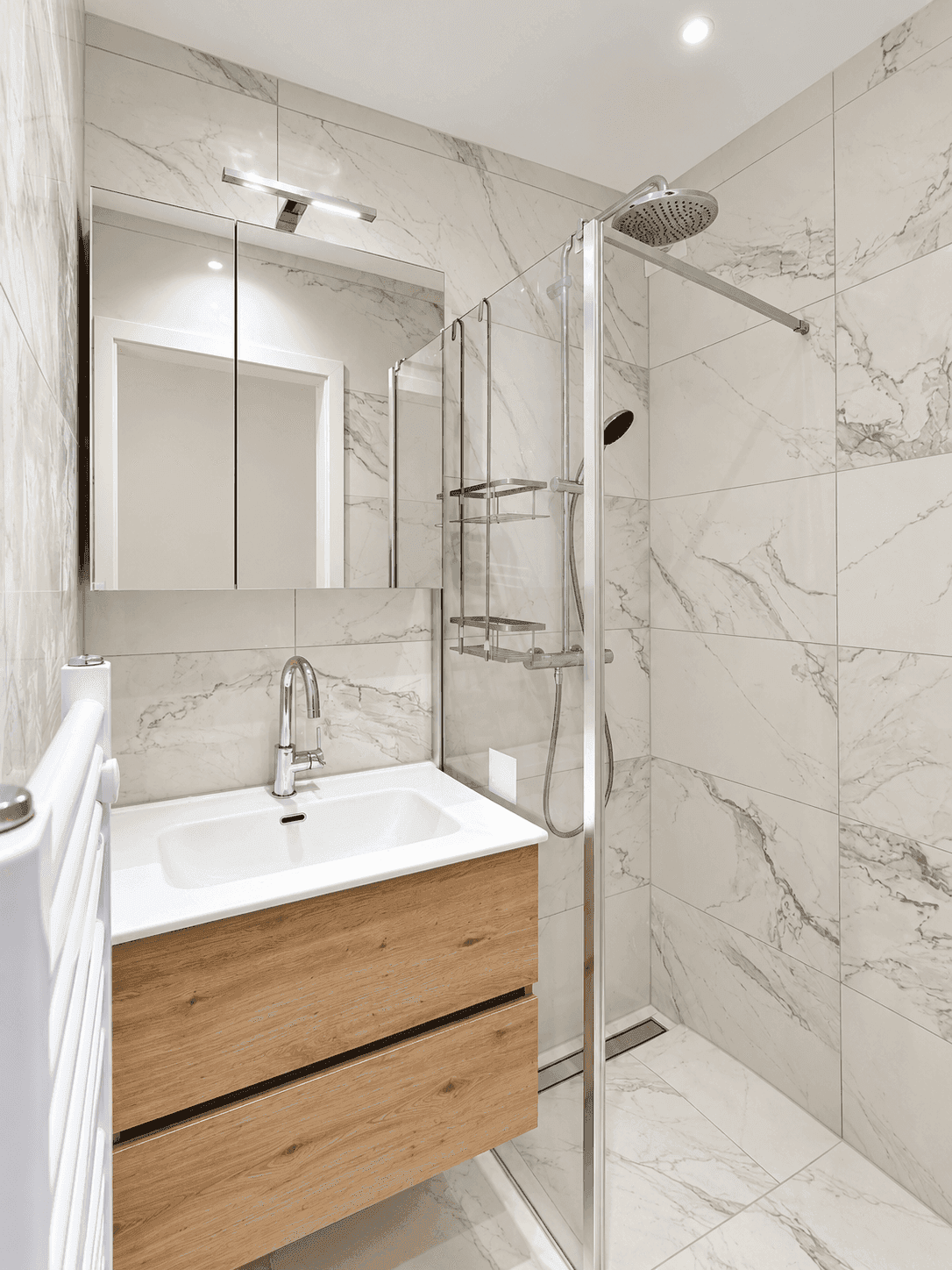 Modernes Badezimmer mit begehbarer Dusche, Holzwaschtisch, Spiegelschrank und eleganten Marmorfliesen an Wänden und Boden.