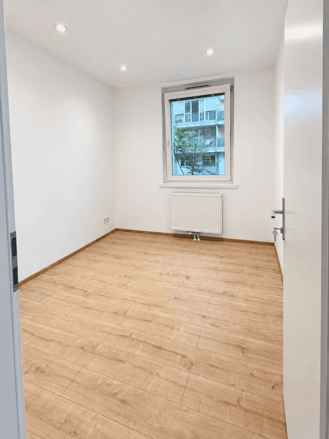 Kleineres, helles Zimmer mit Laminatboden und Fenster, ideal als Kinder- oder Gästezimmer mit Blick ins Grüne.