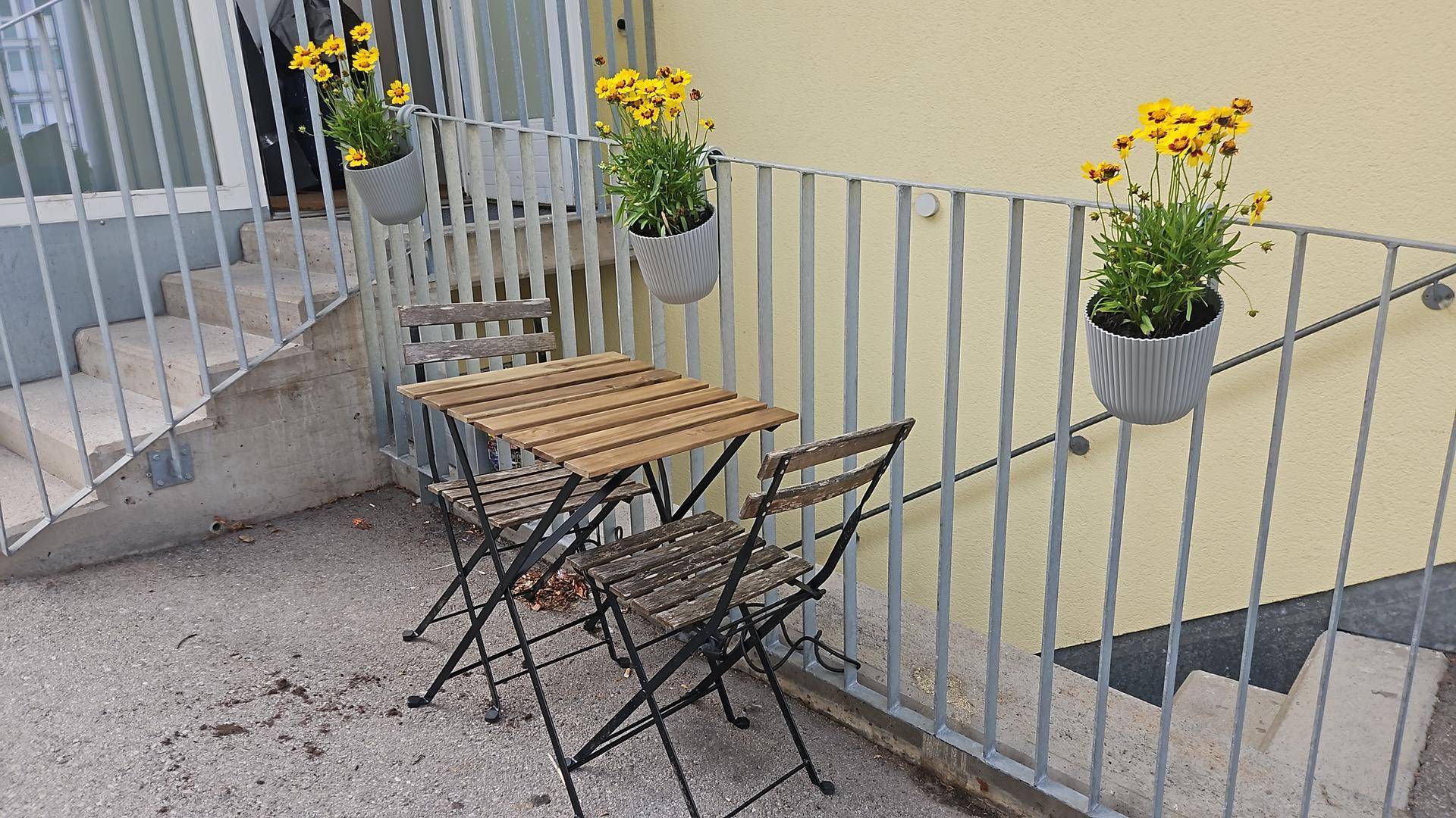 Kleiner Außenbereich mit Holztisch und Stühlen, dekoriert mit Blumen.