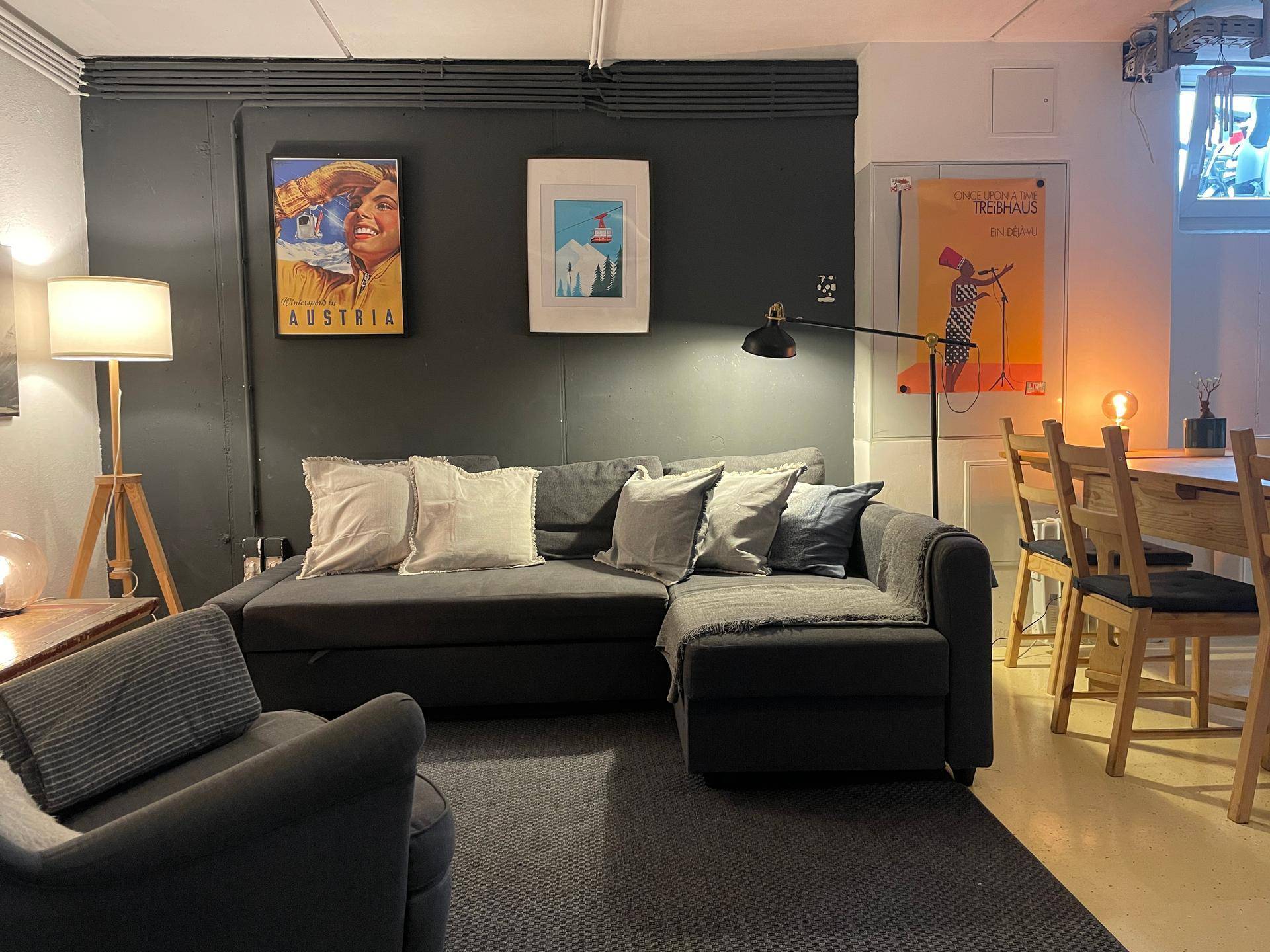 Gemütliche Sitzecke mit dunklem Ecksofa, Stehlampe und Wanddekoration.
