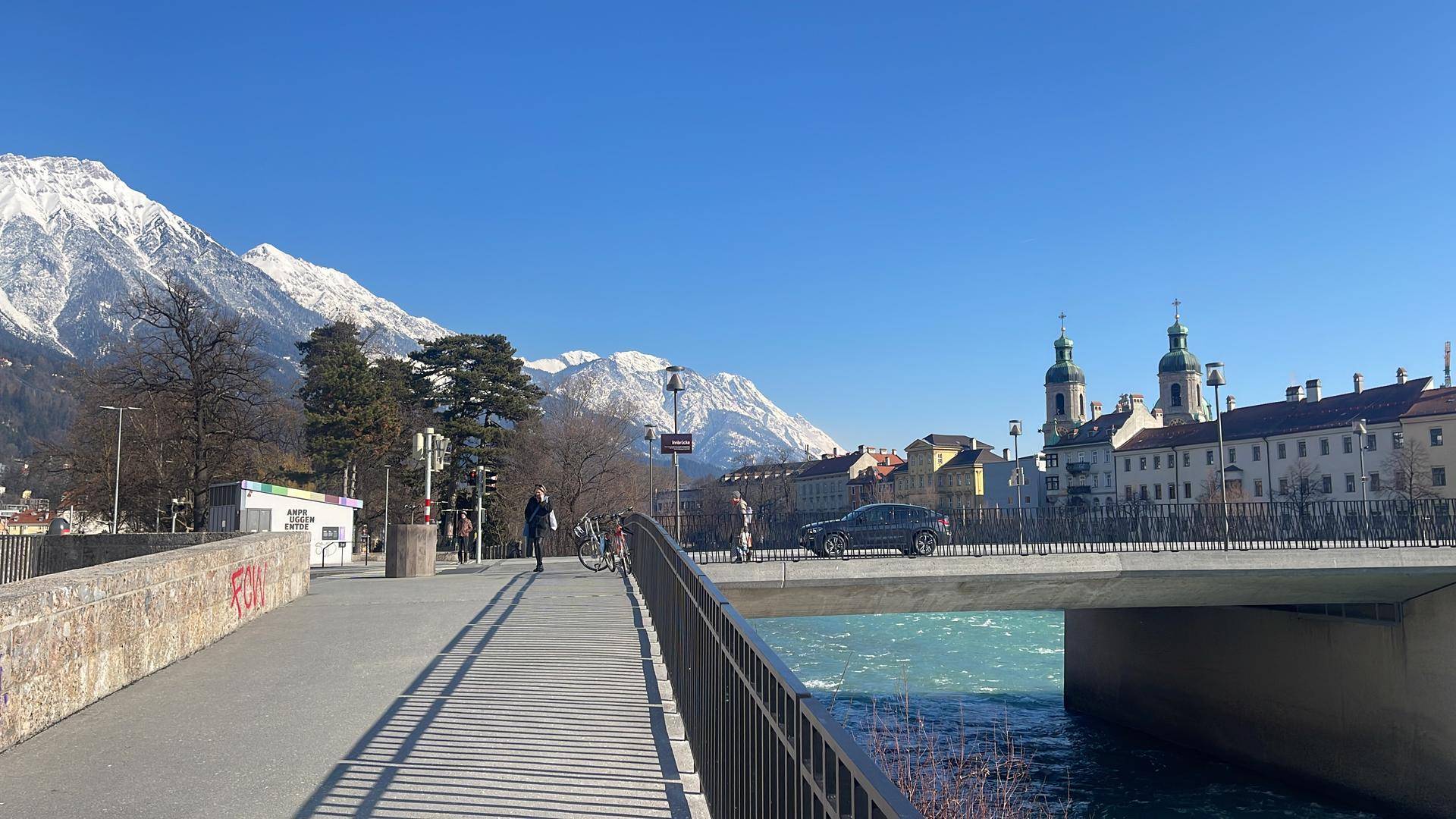 Panoramablick auf die Stadt mit schneebedeckten Bergen und einem Fluss unter blauem Himmel.