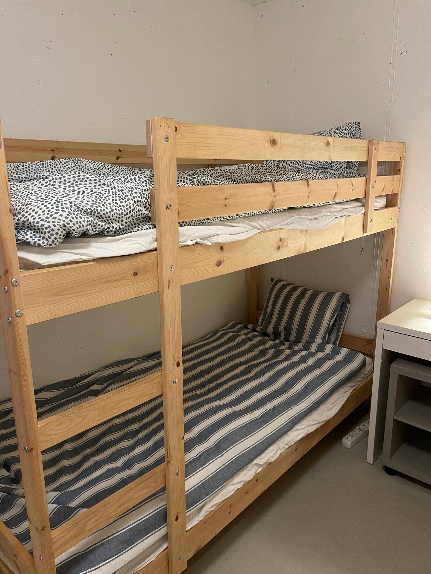 Etagenbetten mit Holzrahmen und unterschiedlichen Bettbezügen in hellem Raum.