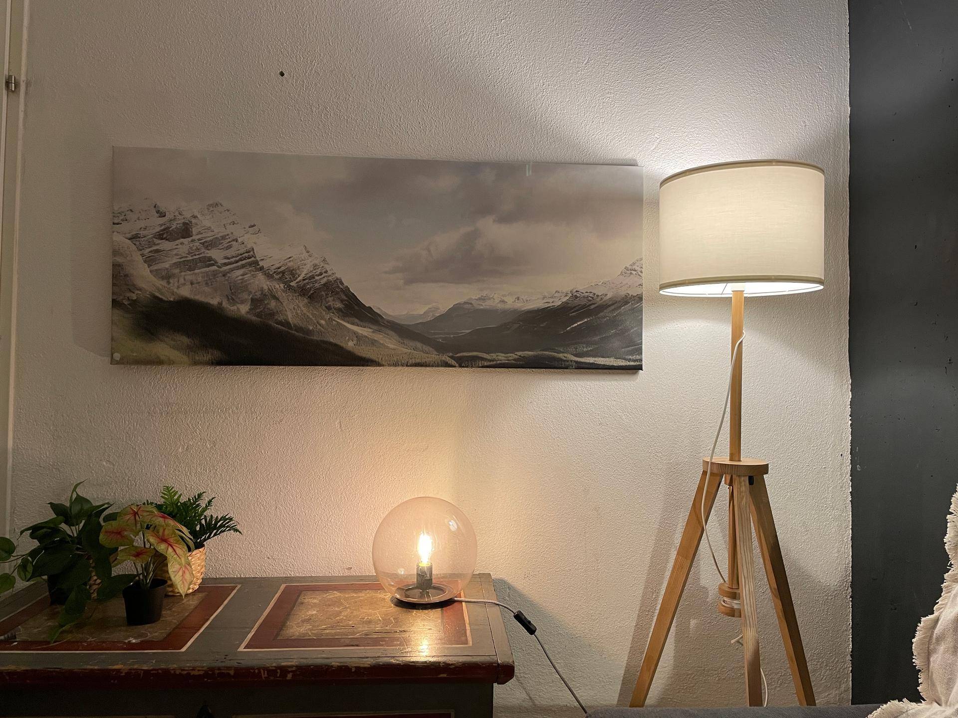 Detailansicht eines Beistelltisches mit Lampe und Wandbild in warmem Licht.