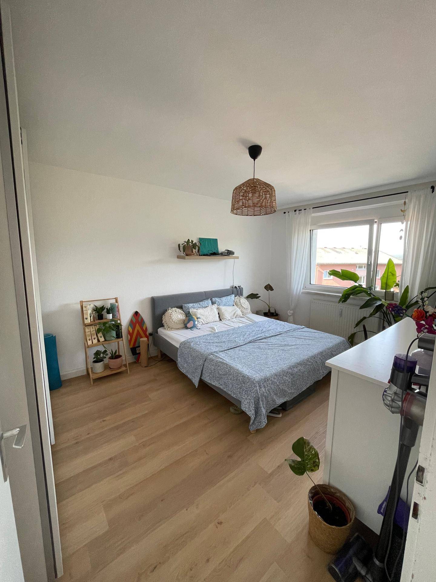 Helles Schlafzimmer mit Doppelbett, Holzboden und großem Fenster.