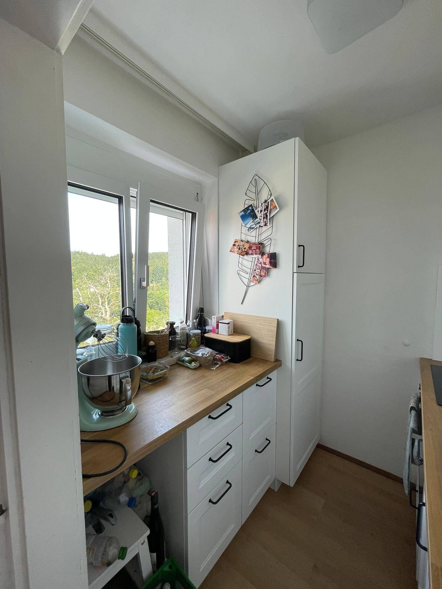 Helle Küche mit Holz-Arbeitsplatte, weißen Schränken und Fenster mit Ausblick.