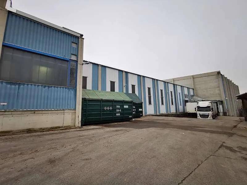 Industriegebäude mit blauen und weißen Fassaden, einem Ladebereich und einem großen grünen Container.