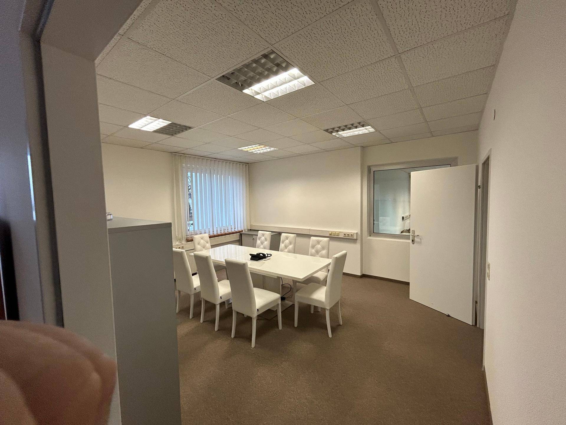 Ein Konferenzraum mit einem großen weißen Tisch und mehreren Stühlen, bereit für Besprechungen.