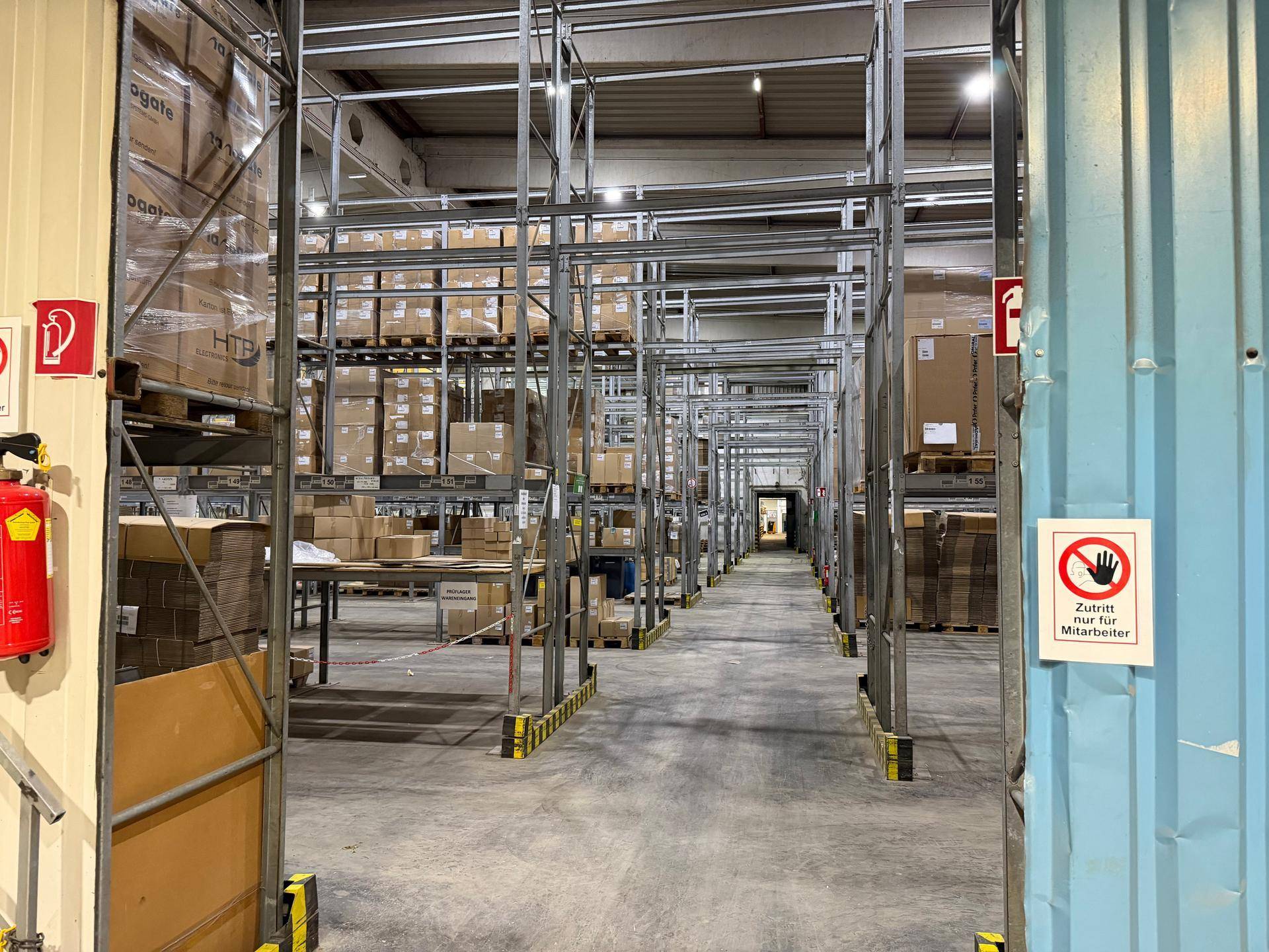 Lagergang mit hohen Regalsystemen, teilweise mit verpackten Waren gefüllt, und Betonboden.