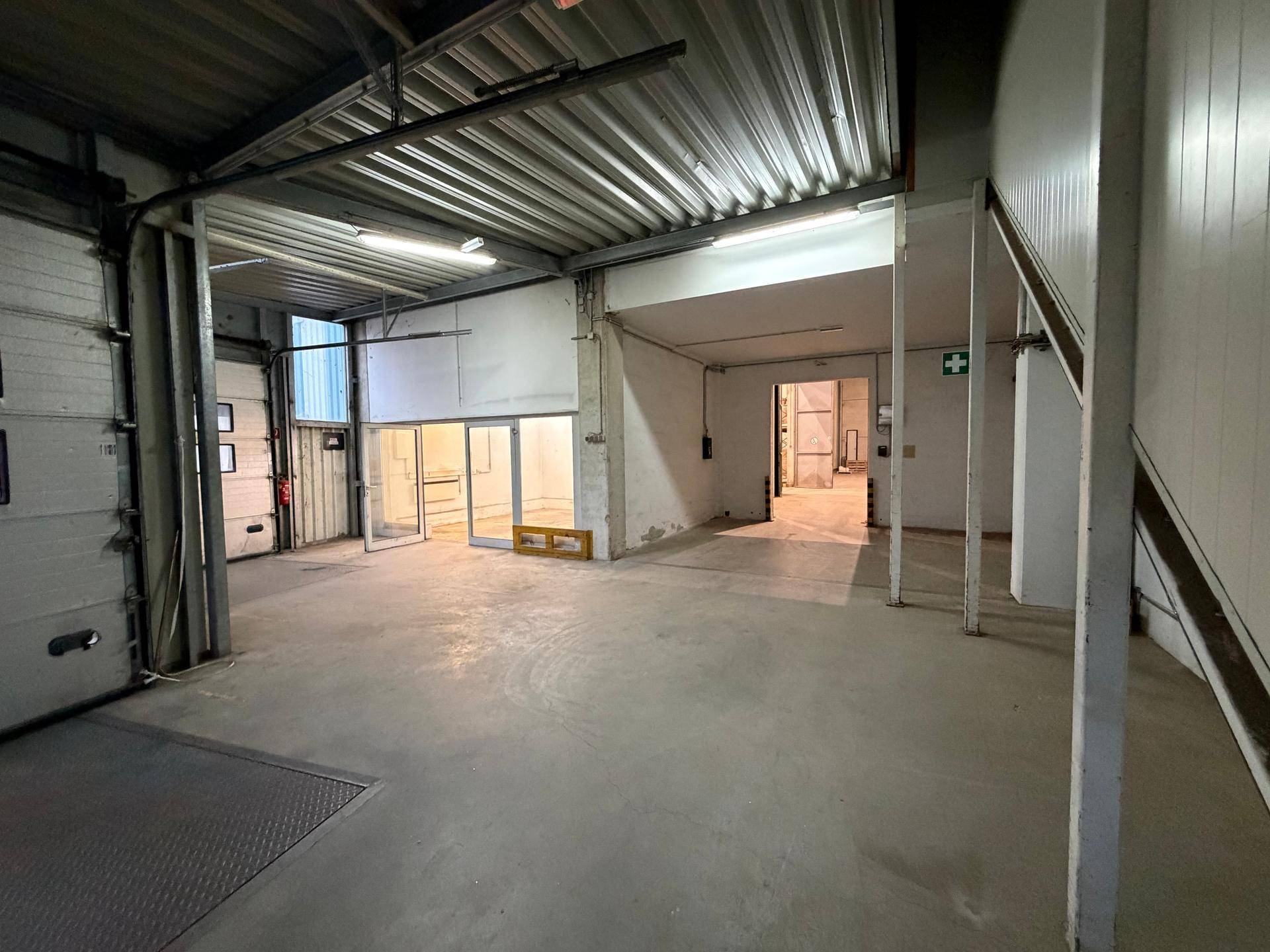Geräumige Lagerhalle mit Betonboden, hohen Decken und großen Rolltoren für den Warenumschlag.