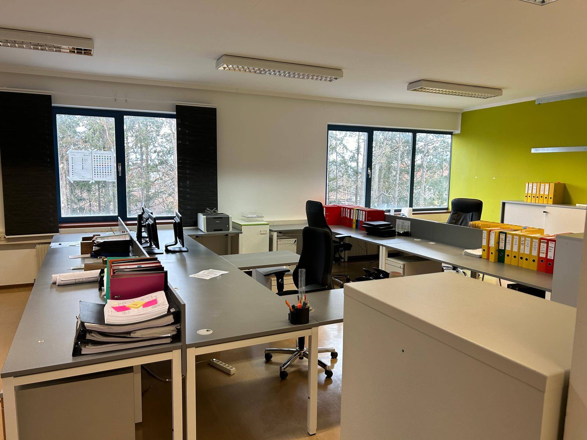 Großraumbüro mit mehreren Arbeitsplätzen, Computern und Blick ins Grüne.