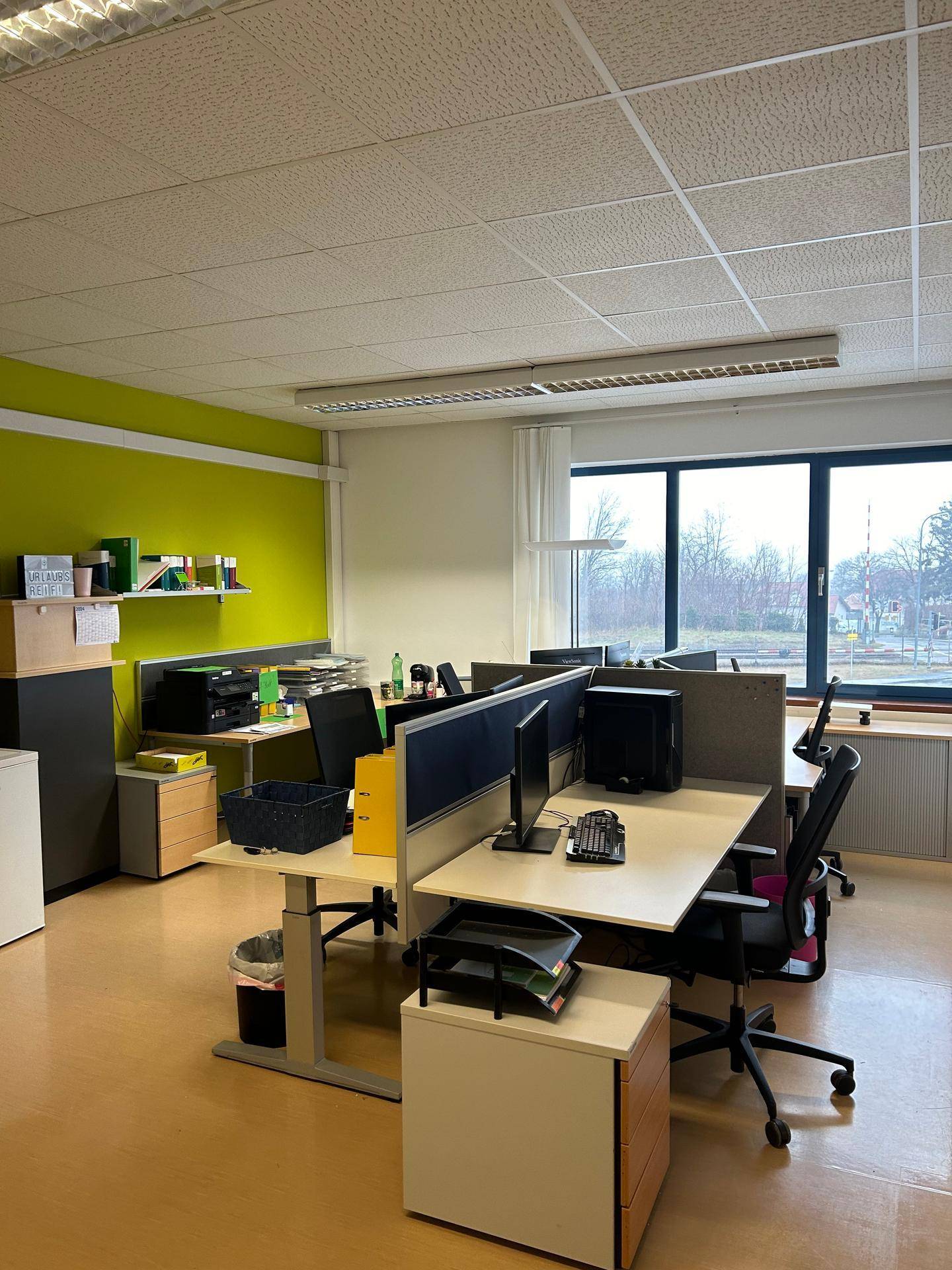 Modern eingerichtetes Büro mit mehreren Arbeitsplätzen und einer auffälligen grünen Wand.