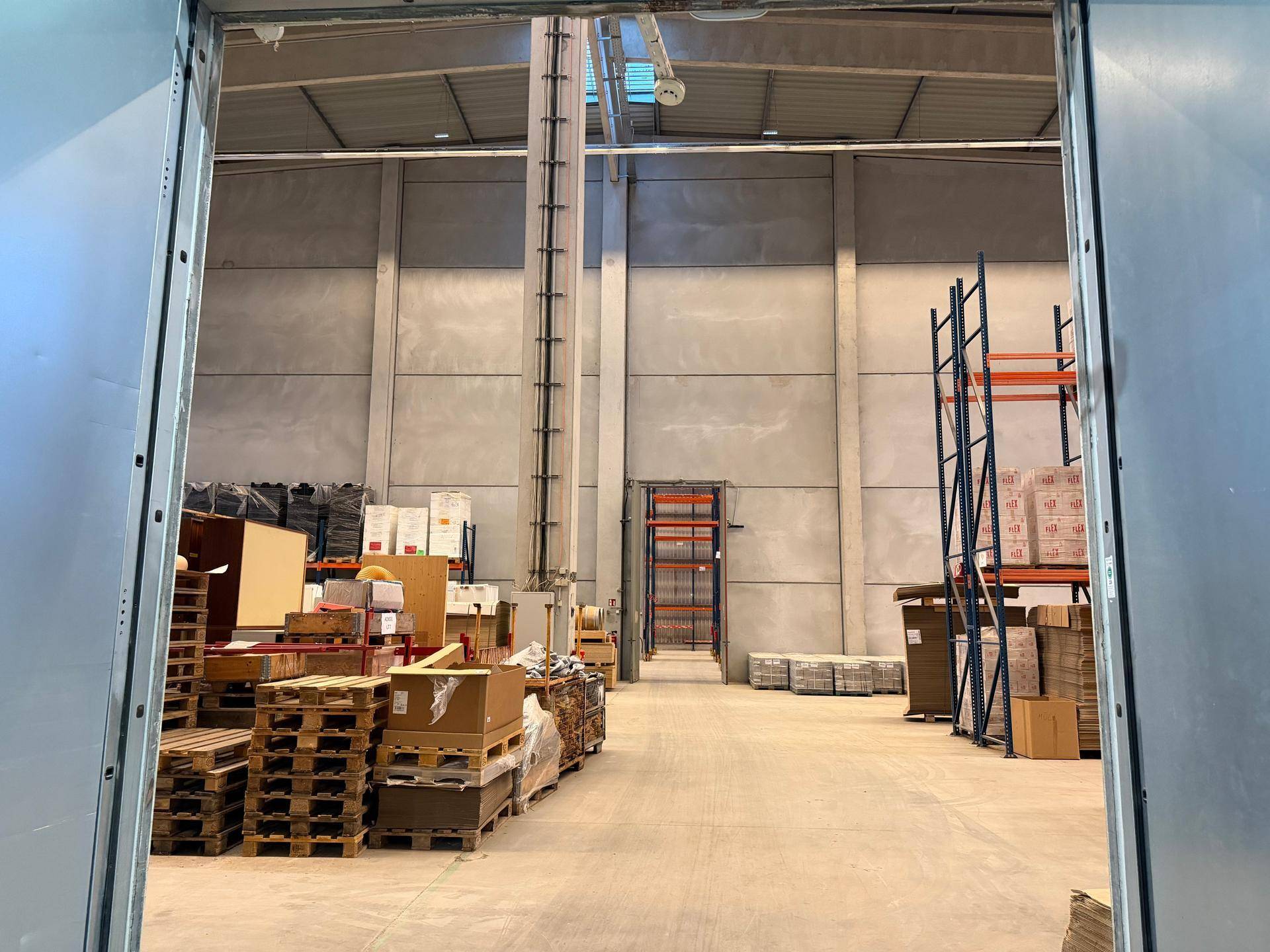 Blick in eine Lagerhalle mit gestapelten Paletten und Waren, durch eine große Öffnung.