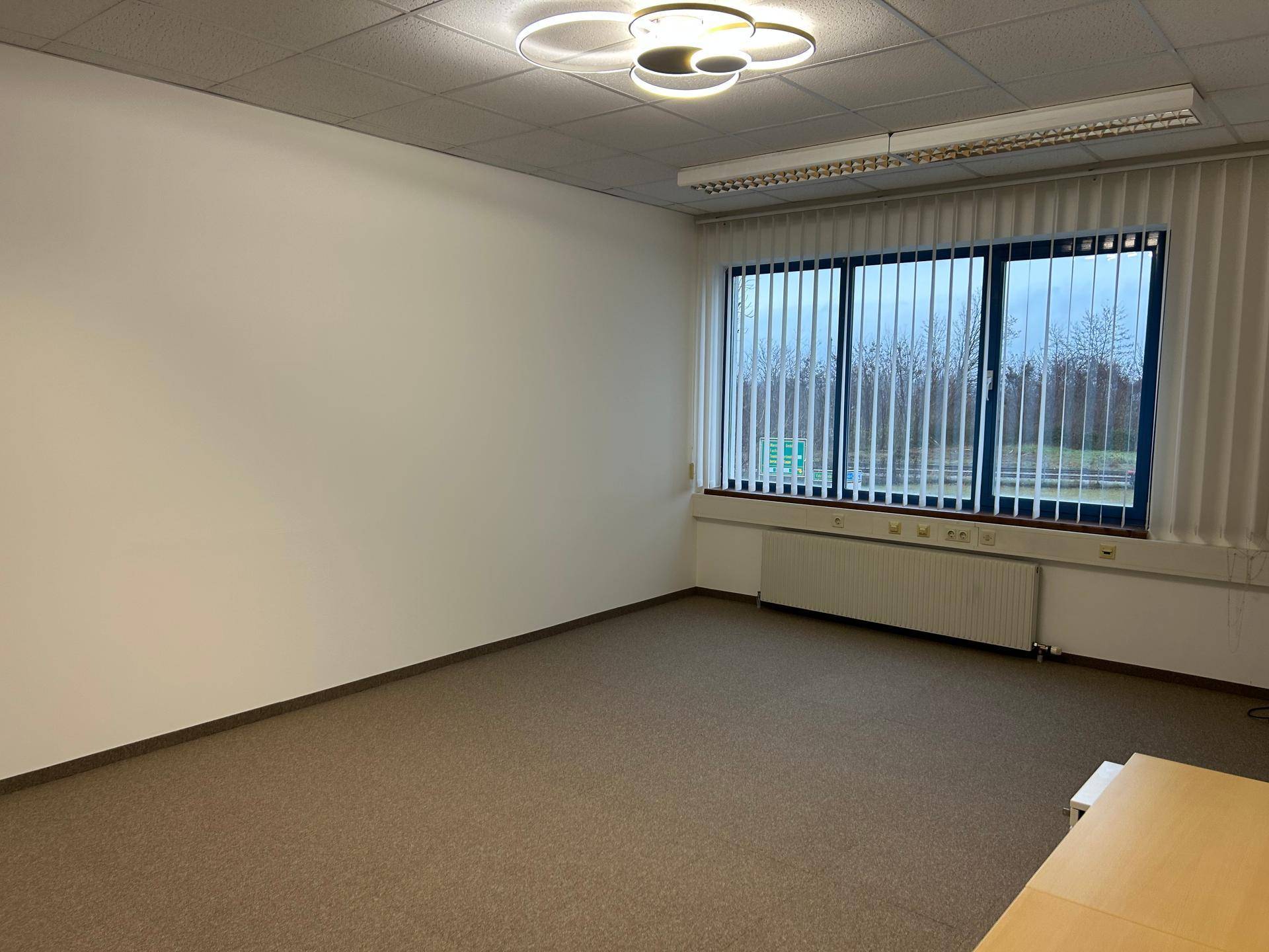 Leeres Büro mit großen Fenstern und vertikalen Jalousien, bietet viel Tageslicht.