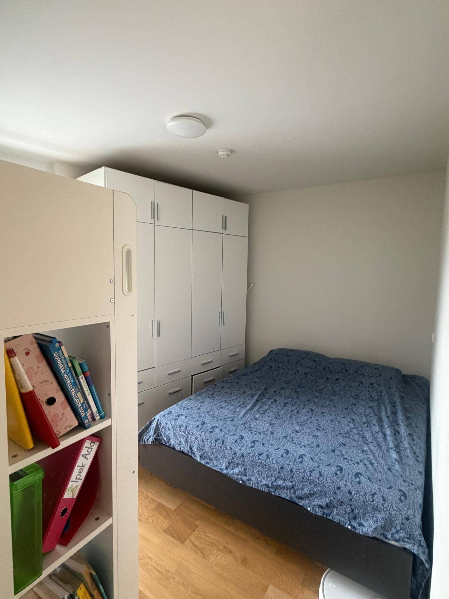 Gemütliches Schlafzimmer mit großem Kleiderschrank, Holzboden und blauem Bettbezug.
