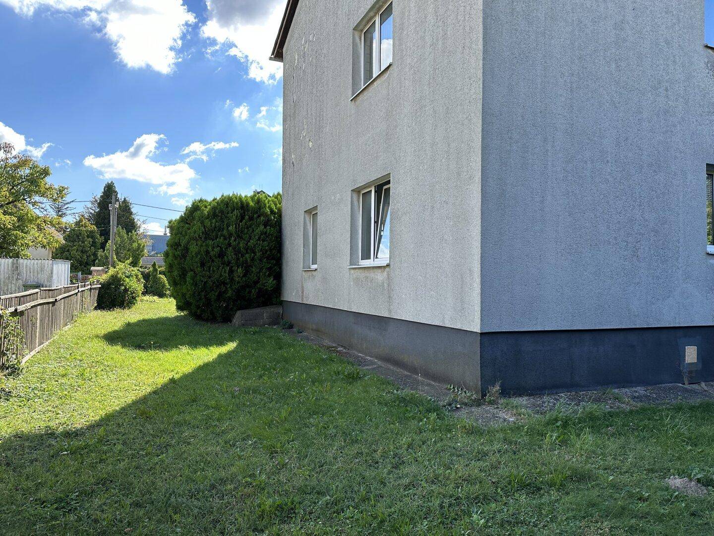 Seitenansicht des Hauses mit gepflegtem Rasen und einem Holzzaun unter blauem Himmel.